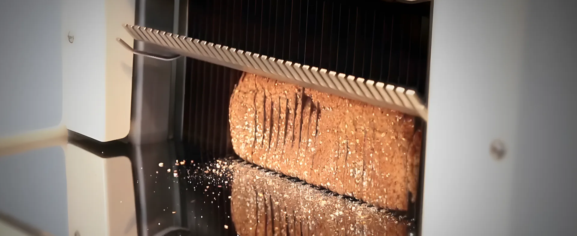 Close-up of the JAC Duro semi-automatic bread slicer during loaf slicing in a professional bakery bread production environment.