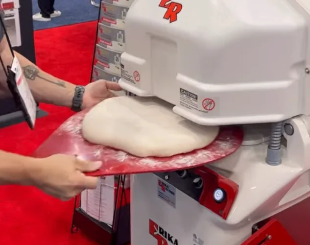 Man inserting a rounding plate with dough into a Full RH divider rounder from Erika Record for dividing and rounder. This is a piece of bakery equipment.