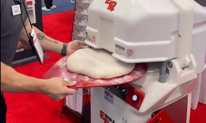 Man inserting a rounding plate with dough into a Full RH divider rounder from Erika Record for dividing and rounder. This is a piece of bakery equipment.