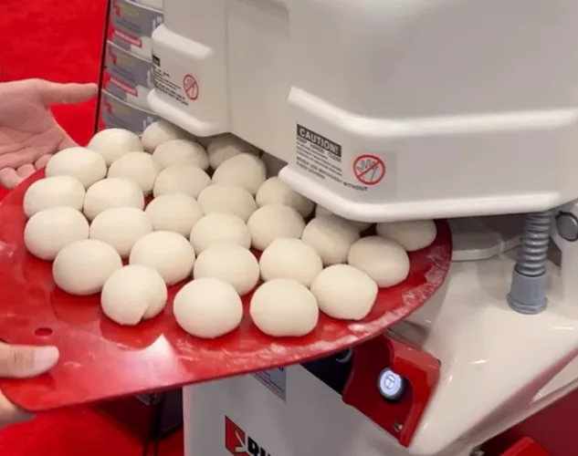 Perfect round dough balls on a red plastic rounding plate being removed from an Erika Record FULL RH automatic dough divider rounder, a piece of bakery equipment.