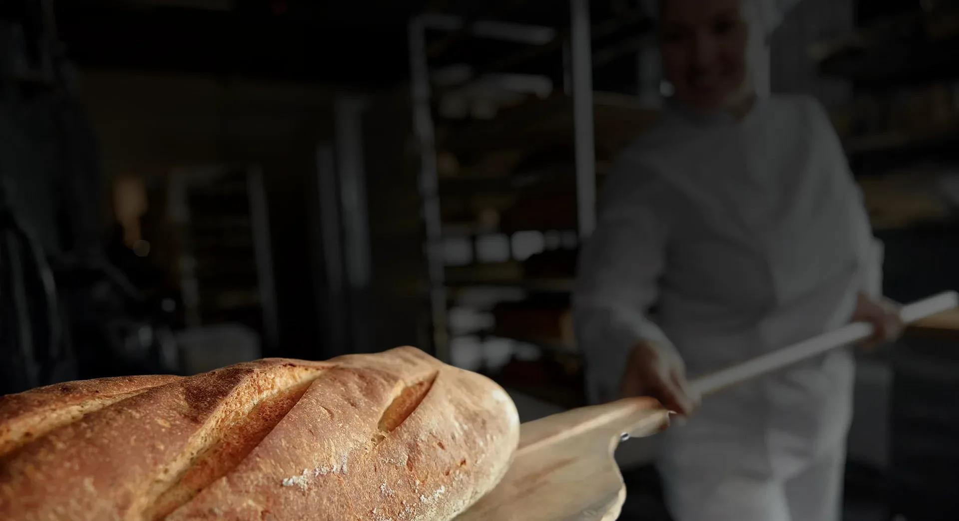 Baker removing a loaf of artisan bread from a commercial oven using professional bakery equipment.