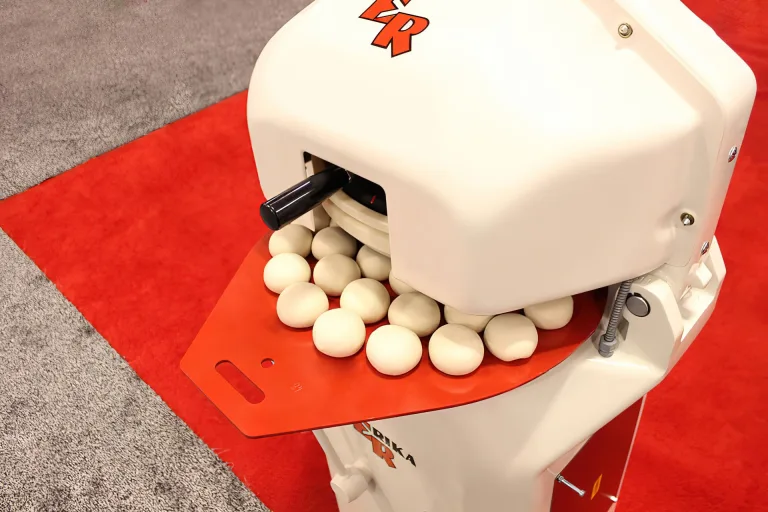 Evenly rounded dough balls resting on the red tray of a white Erika Record Semi RH divider rounder. Divider rounders are where Erika Record Baking Equipment got its start in 1991.